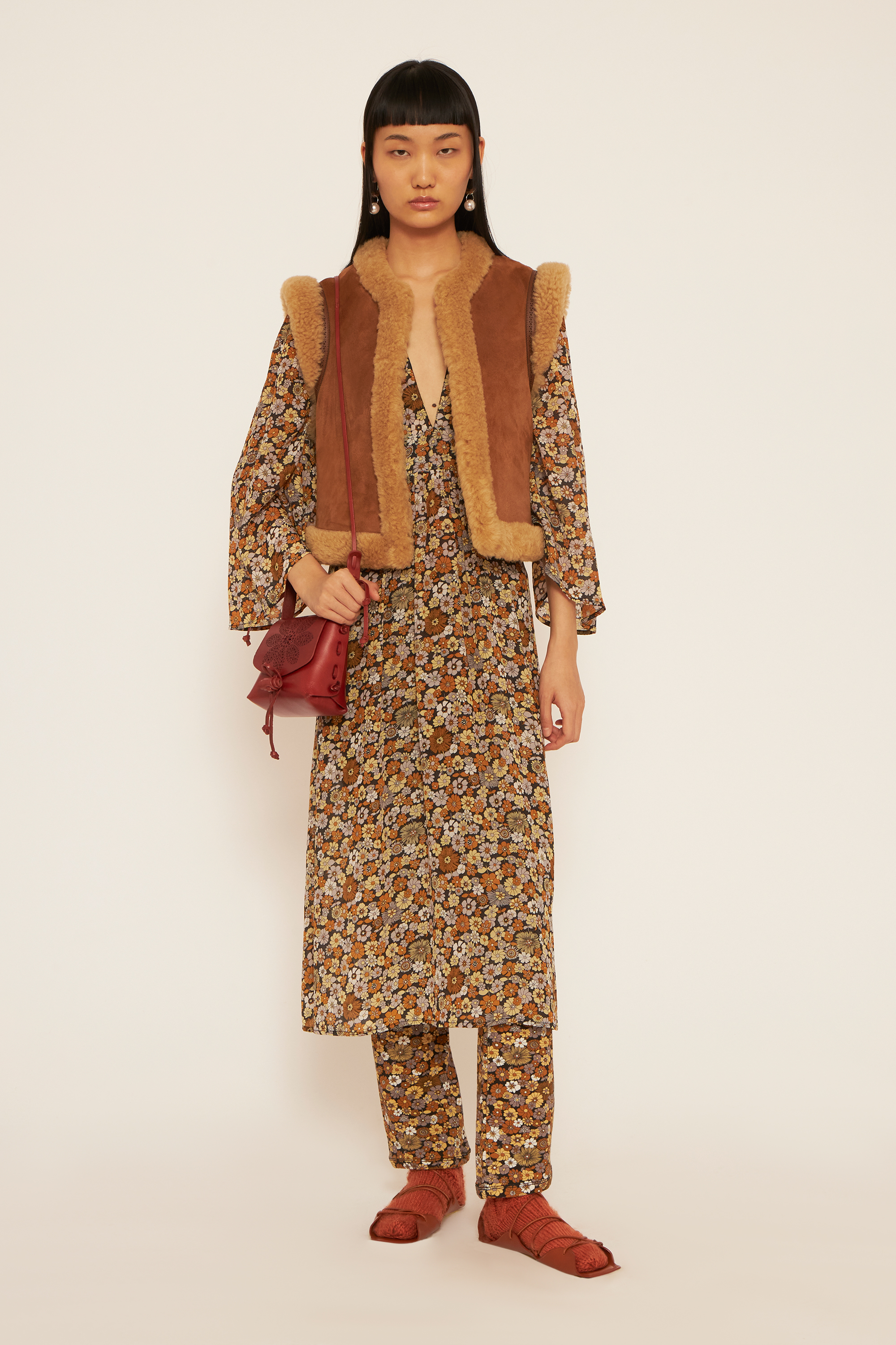 A girl wearing a fur gilet, a flower printed longdress, a flower printed leggings and socks with sandals.