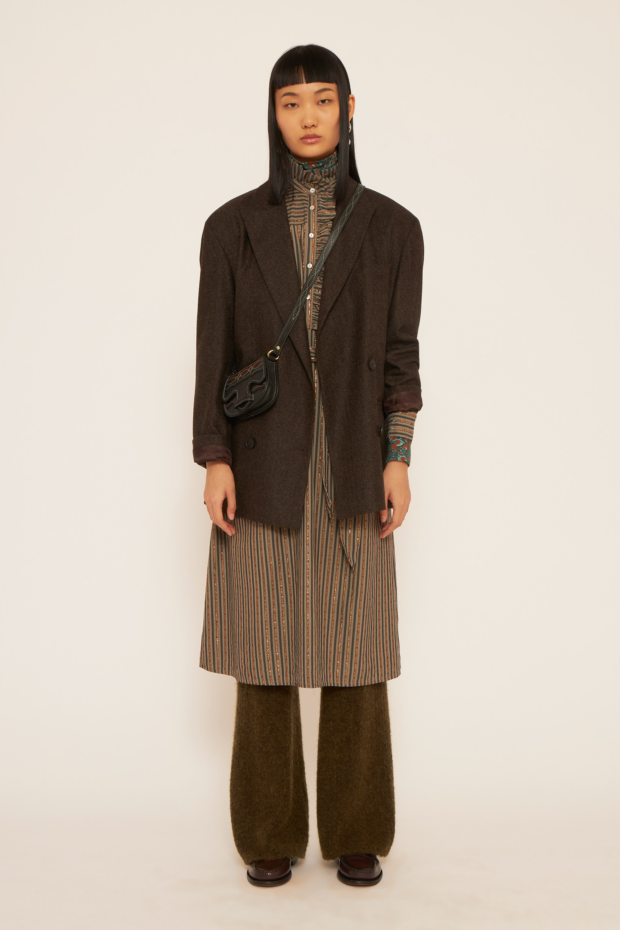 A girl wearing a brown jacket, a kaki dress and a craft brown pants.