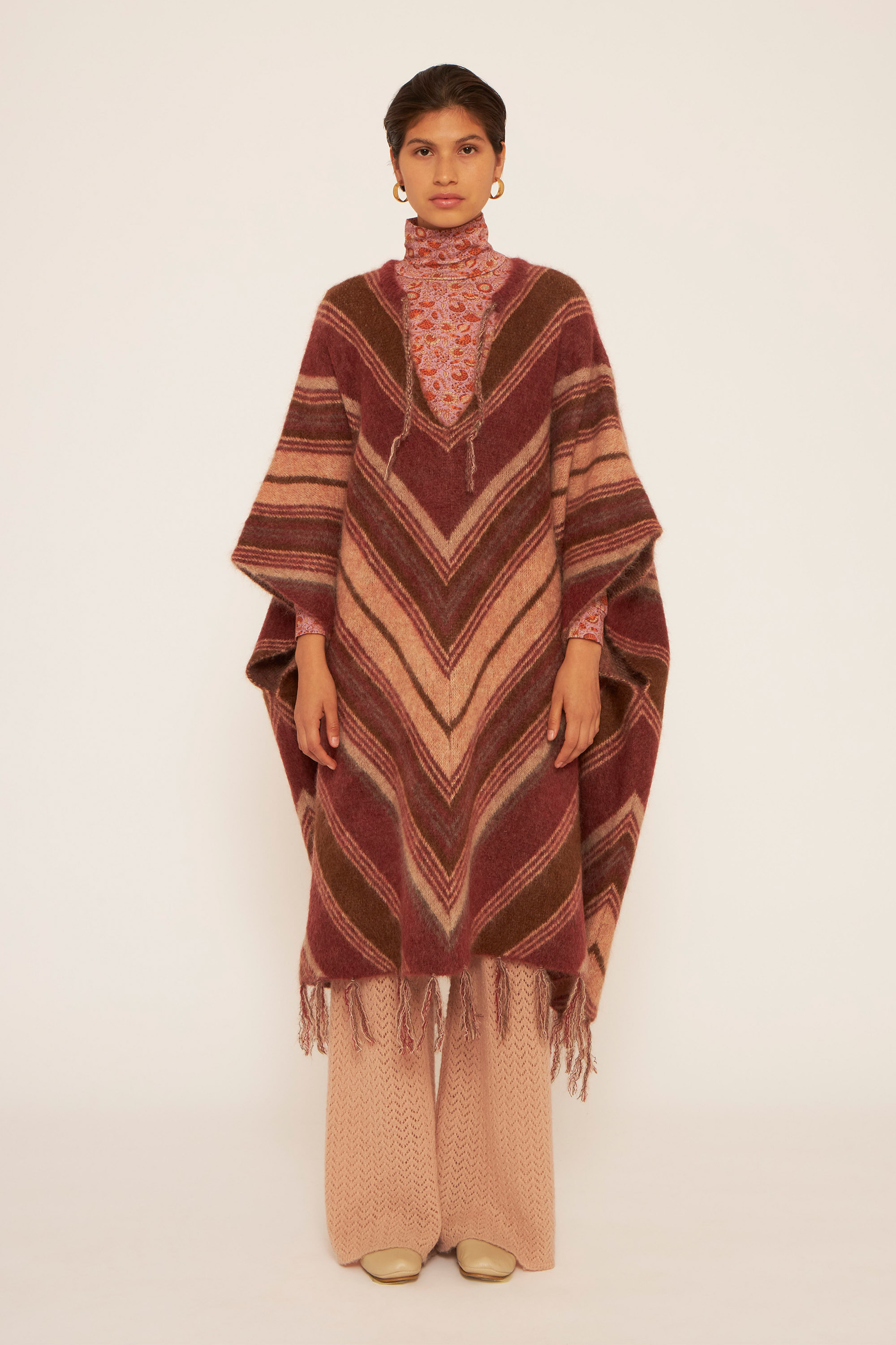 A girl wearing a long poncho in shade of burgundy, a craft light pink pants and a pink printed t-neck.
