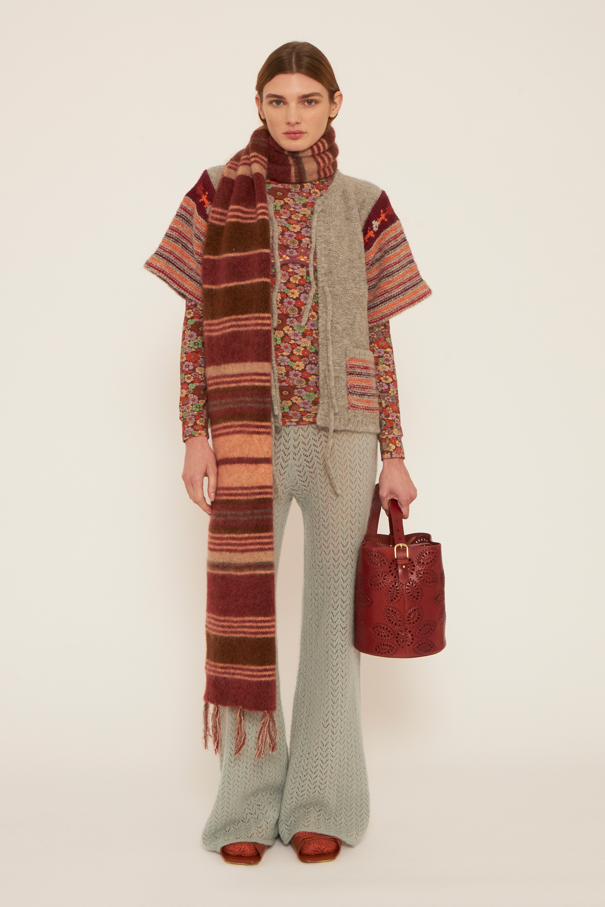 A girl wearing a craft light blue pants, a flower printed t-neck, a grey cardigan and a big burgundy shades scarf.